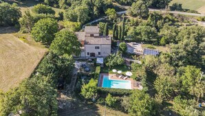 An aerial view of a property with a swimming pool, surrounded by lush greenery and a hilly landscape.