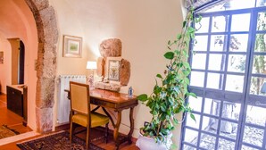 A dining area with a rustic stone wall, a wooden table, a chair, a potted plant, and a window with a view of the outdoors.