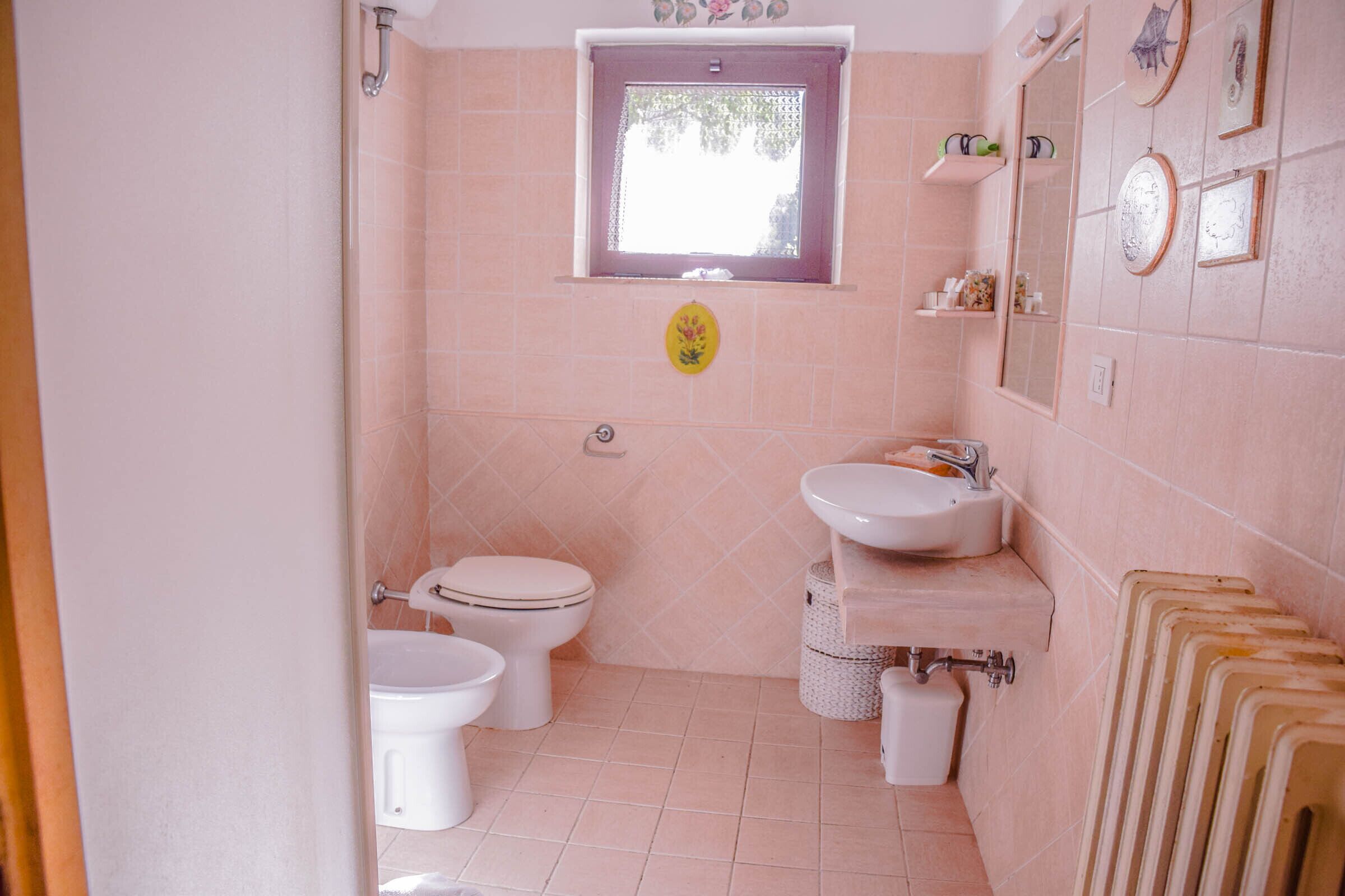 A bathroom with two toilets, a sink, a window, and a radiator.
