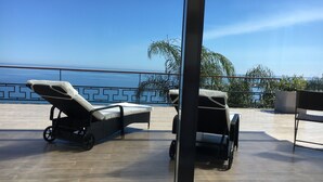 Ein Balkon mit zwei Liegestühlen und einer Sitzbank, mit Blick auf ein Gewässer.