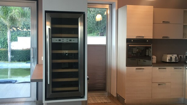 Eine moderne Küche mit Edelstahlgeräten, Holzschränken und einem großen Fenster mit Blick auf Grünflächen.