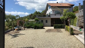 Ein modernes, zweistöckiges Haus mit Schotterauffahrt, umgeben von viel Grün und blauem Himmel.