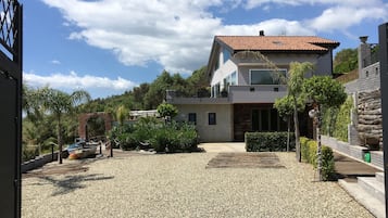 A modern two-story house with a gravel driveway, surrounded by greenery and a clear sky.