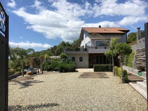 Una casa moderna de dos pisos con camino de grava, rodeada de vegetación y un cielo despejado.