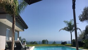 Ein Schwimmbad mit Blick auf den Ozean, umgeben von Palmen und einem Gebäude mit einem Balkon.
