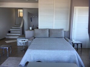 Un dormitorio con una cama grande, una mesita pequeña, una silla, una escalera y un baño a la vista al fondo.