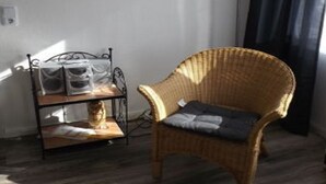 A room with a wicker chair, a framed picture on the wall, a floor lamp, and a metal shelf with bags. - Bright and modern apartment right on the North Sea (Nordstrand)