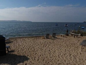 Ein Sandstrand mit einigen Liegestühlen und einer kleinen Struktur, vermutlich ein Grillplatz.