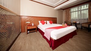 A hotel room with a large bed, a wooden headboard, a nightstand with a lamp, a small table with a fruit bowl, and a chair. - OYO 8027 Li Hu Business Hotel (Shenzhen)