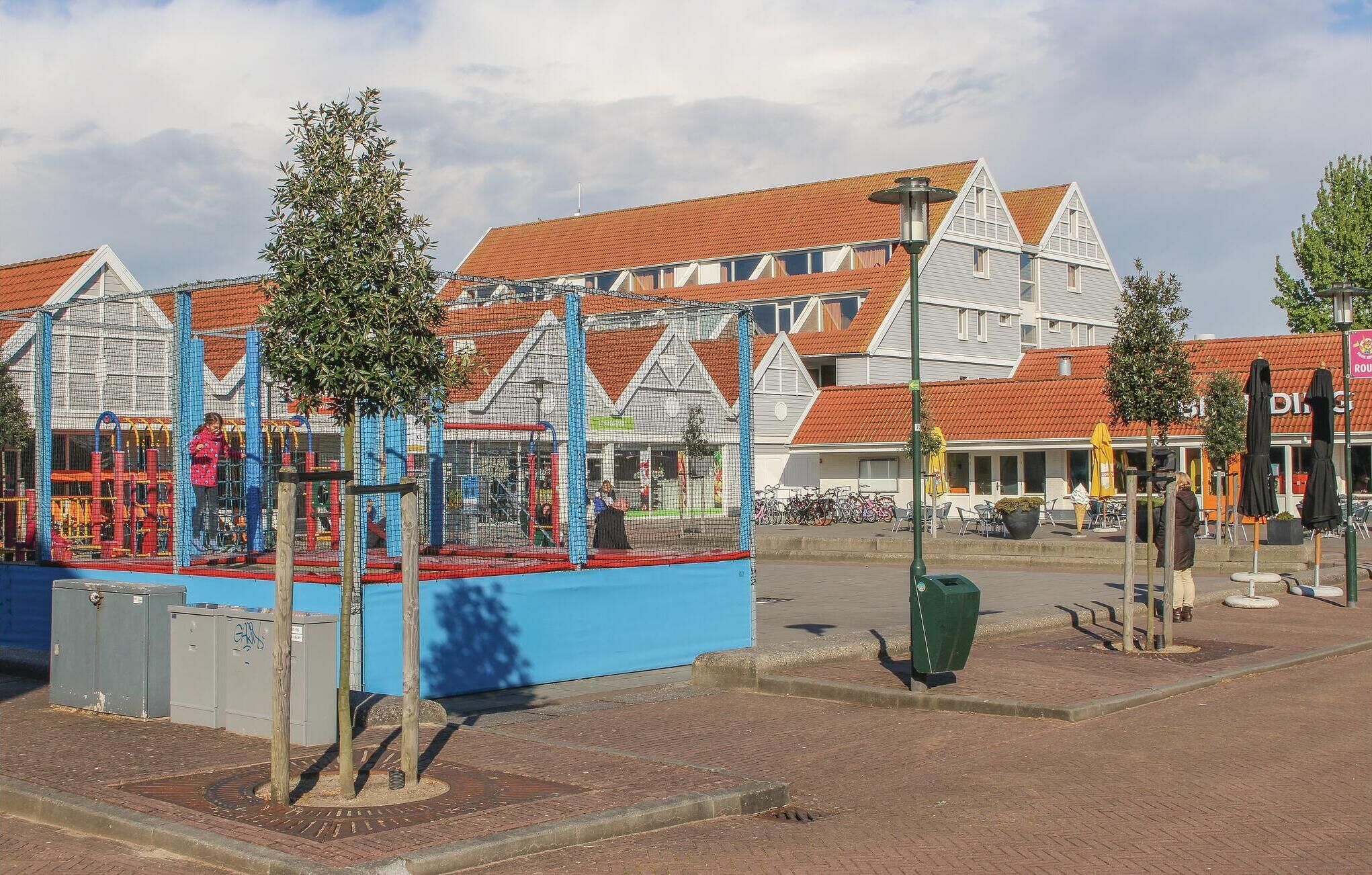 A playground with climbing structures and a fenced area, surrounded by buildings with red-tiled roofs and white facades.