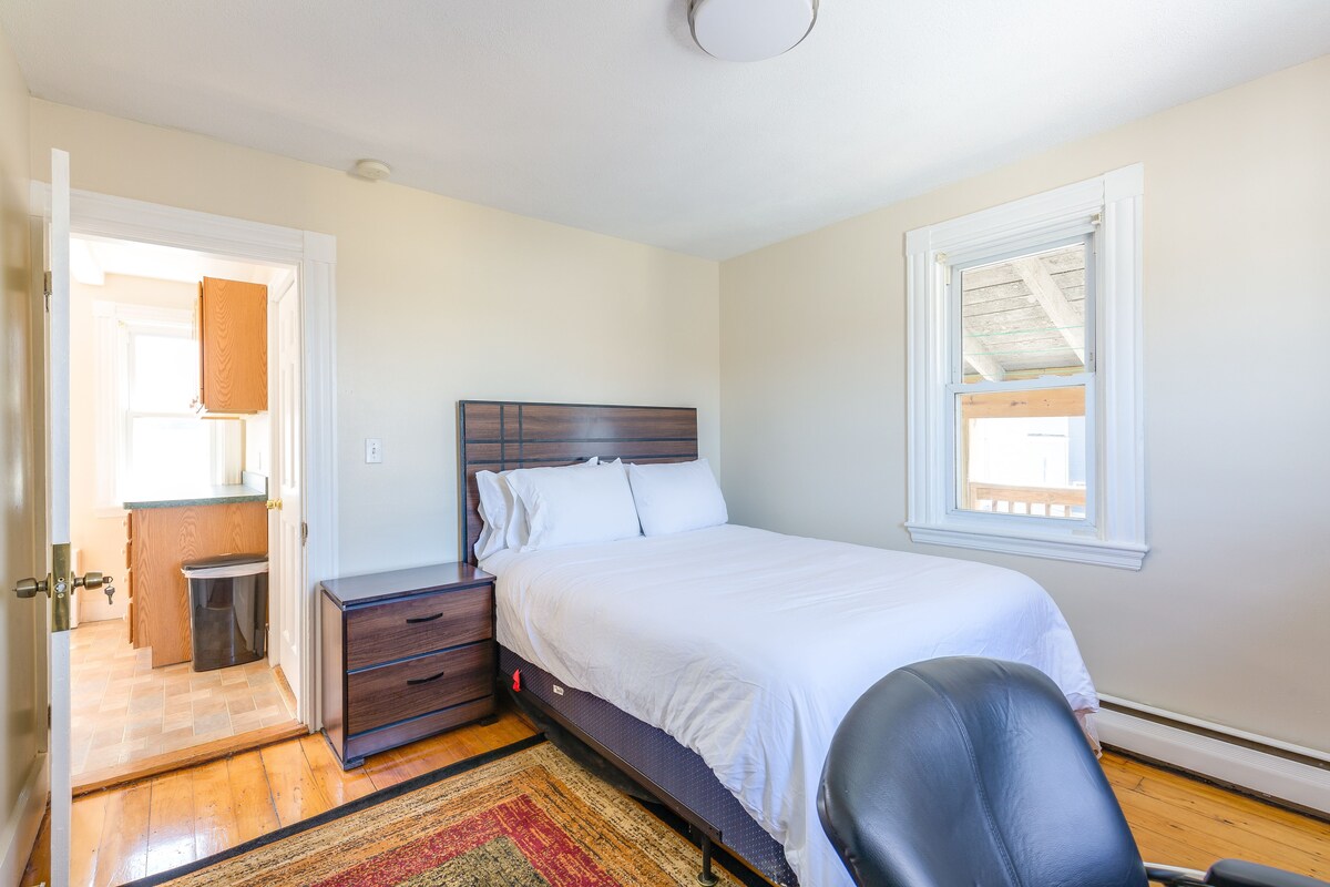 A bedroom with a bed, a desk, a chair, and a window.