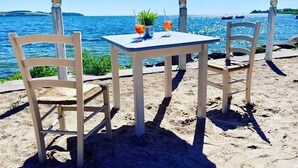 A beachside table with two chairs and a small table, overlooking a calm sea with boats in the distance. - Apartment 2 - Ahoi-Marie (Middelhagen)