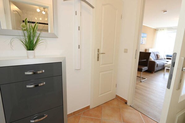 Un interior moderno con una puerta blanca, una planta en maceta y un mueble gris con cajones.