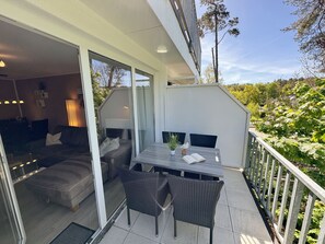 Un espacio exterior moderno con puerta de vidrio que da a un interior acogedor, una mesa de comedor con sillas y vista a un jardín exuberante.