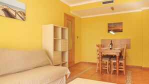 A yellow-walled room with a beige sofa, a wooden dining table with chairs, and a white cabinet. - 2 bedroom lovely apartment in Piles (Piles)