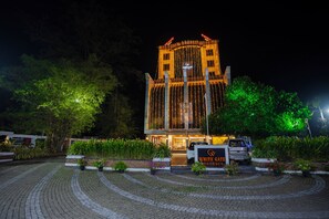 Um edifício com uma placa indicando "WHITE GATE RESIDENCY" à noite, rodeado por vegetação e um espaço pavimentado.