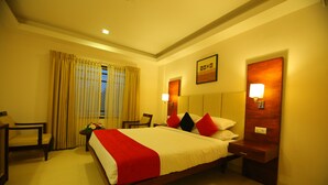 A hotel room with a large bed, two bedside tables, a chair, and a window with curtains. - White Gate Residency (Vaikom)