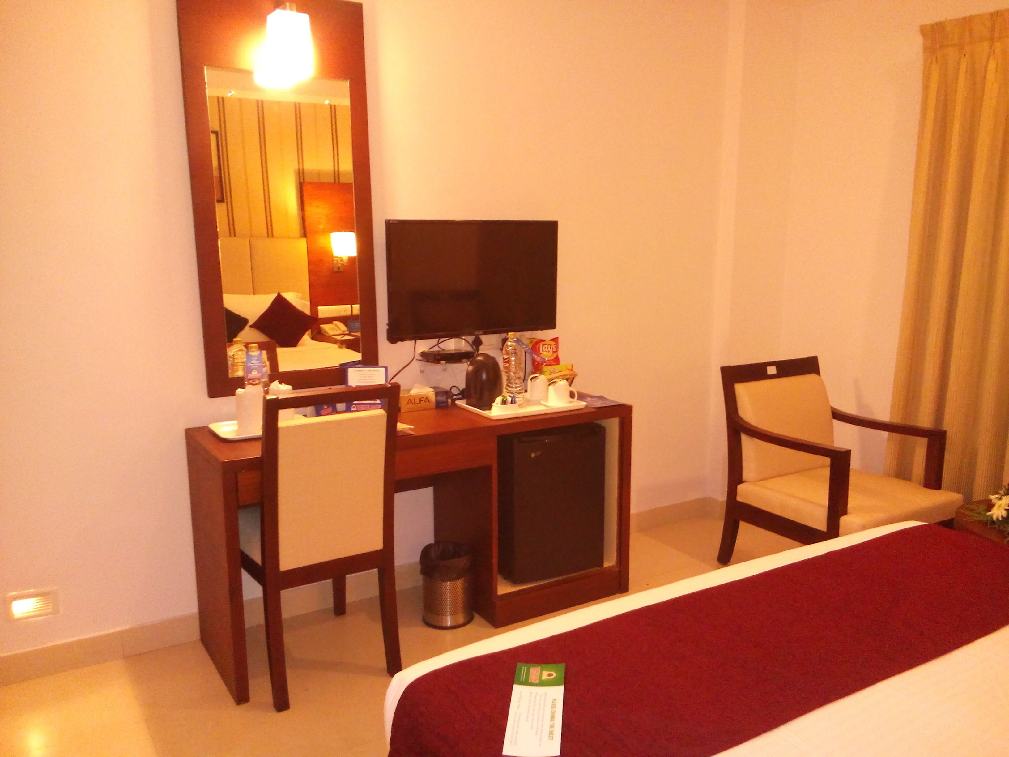 A hotel room with a bed, a desk with a computer, a chair, and a small cabinet.