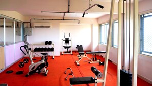 A gym with exercise equipment, a bench, dumbbells, and a red carpet floor. - White Gate Residency (Vaikom)