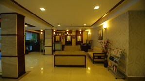 A hotel lobby with a reception desk, sofas, a coffee table, and a magazine rack. - White Gate Residency (Vaikom)