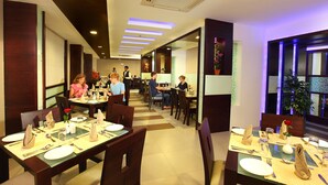 A restaurant with multiple dining tables, each set with plates, cutlery, and napkins. - White Gate Residency (Vaikom)