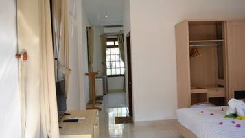 A hotel room with a bed, a wooden wardrobe, a desk with a chair, and a window with curtains.