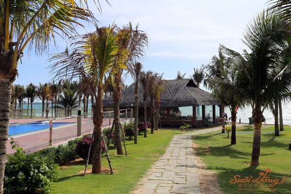 A resort with a pool, palm trees, and a thatched-roof building.