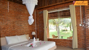 Habitación de hotel con pared de ladrillo, una cama grande con ropa blanca, una ventana con cortinas y vistas a un jardín.