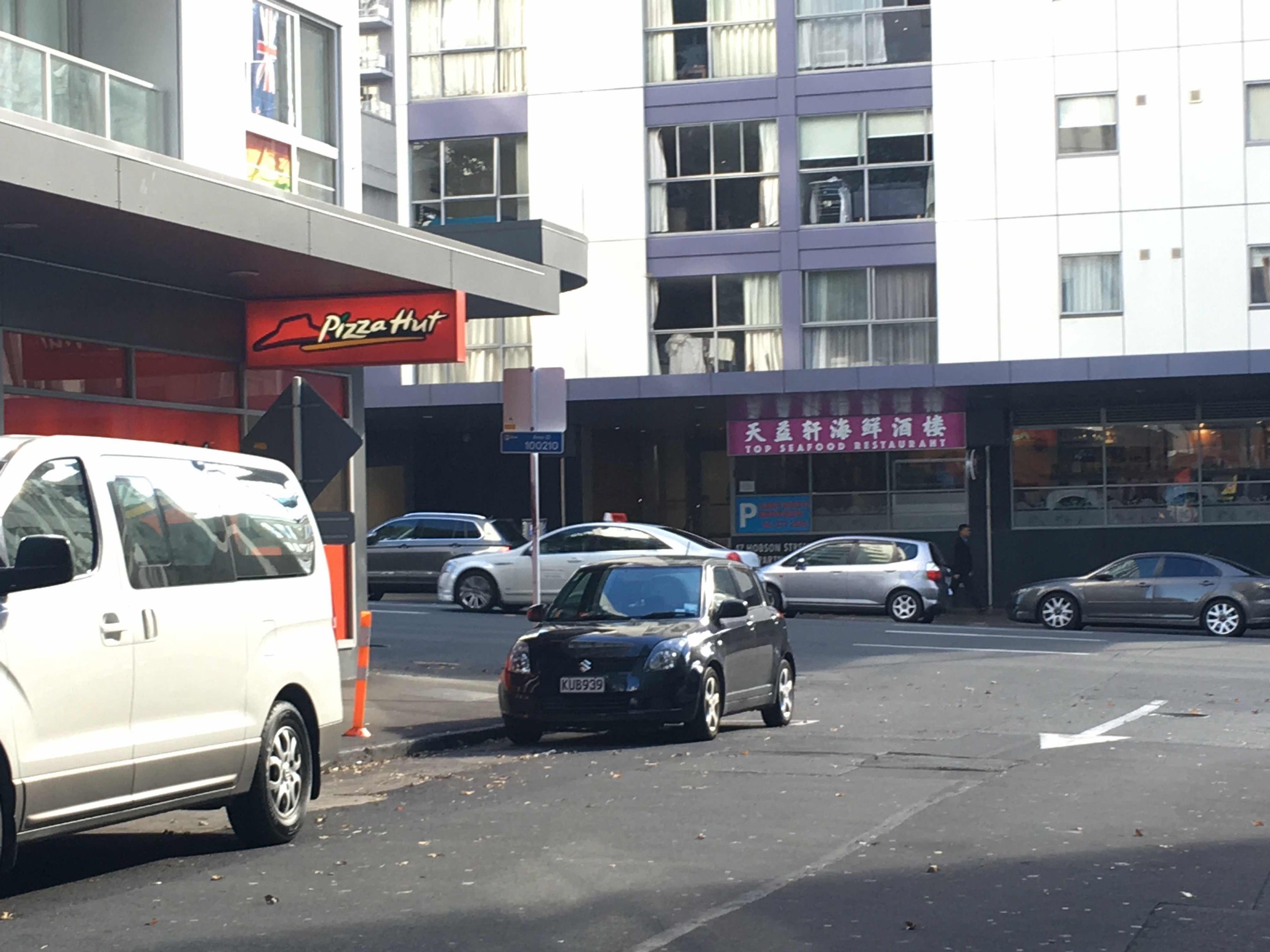 A parking lot with several cars, a white van, and a building with a Pizza Hut sign.