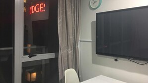 A hotel room with a large flat-screen TV mounted on the wall, a window with a view of the outside, and a curtain. - Altitude (Auckland)