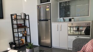 A modern kitchen with a stainless steel refrigerator, a built-in oven, and a microwave. There is a small dining area with a table and chairs. - Altitude (Auckland)