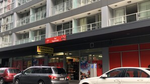 A multi-story building with a storefront for 'Sui Superette Groceries' and 'Coca-Cola' signage. There are parked cars in front. - Altitude (Auckland)