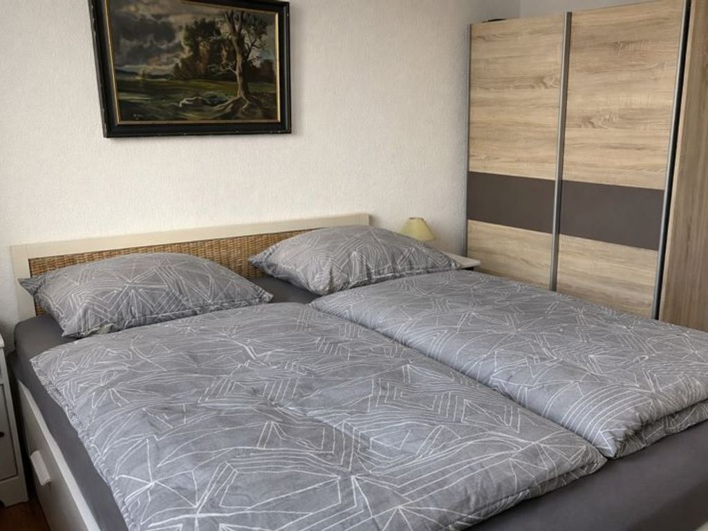 A bed with a geometric patterned bedspread and pillows, a nightstand with a lamp, and a wardrobe with a striped design.