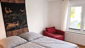 A bedroom with a bed, a red chair, and a tapestry. - Apartment 7 - Ahoi-Marie (Middelhagen)