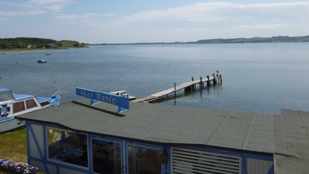 A calm lake with boats, a pier, and a building with a sign reading "Alai Marie". - Apartment 7 - Ahoi-Marie (Middelhagen)