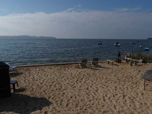 A sandy beach with a few lounge chairs and a small structure, likely a barbecue area.