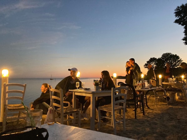 A beachside restaurant with outdoor seating, tables, chairs, and a view of the sea.