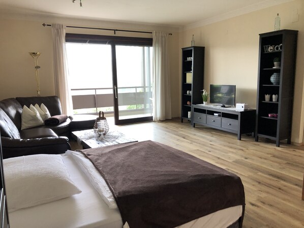 A modern bedroom with a large bed, a TV, a bookshelf, and a balcony.