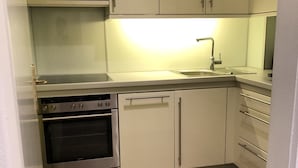 A compact kitchen with white cabinets, a stainless steel oven, a dishwasher, and a sink with a faucet. - Sunny 2 room apartment with a fantastic view of Lake Millstatt (Millstatt)