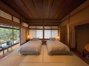 A traditional Japanese-style room with tatami flooring, two beds, a sliding door, and a view of a garden. - Shimizu Ryokan (Yufu)