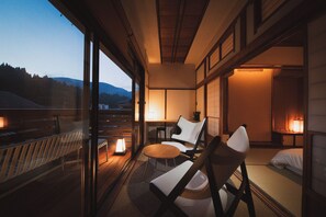A room with a balcony, a bed, a chair, a table, and a nightstand with a lamp. - Shimizu Ryokan (Yufu)