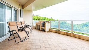 A balcony with four lounge chairs, a built-in grill, and a view of lush greenery. - Seaside KLATCH -Villa & Sauna- (Ishigaki)
