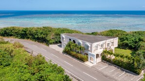 A coastal building with a paved road in front, surrounded by greenery and overlooking the ocean. - Seaside KLATCH -Villa & Sauna- (Ishigaki)