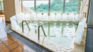 A hot tub with a stone border and a view of the outdoors through a large window. - Seaside KLATCH -Villa & Sauna- (Ishigaki)