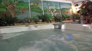Un espace avec un bain à remous, agrémenté d’une fresque représentant des cerfs et un paysage forestier.