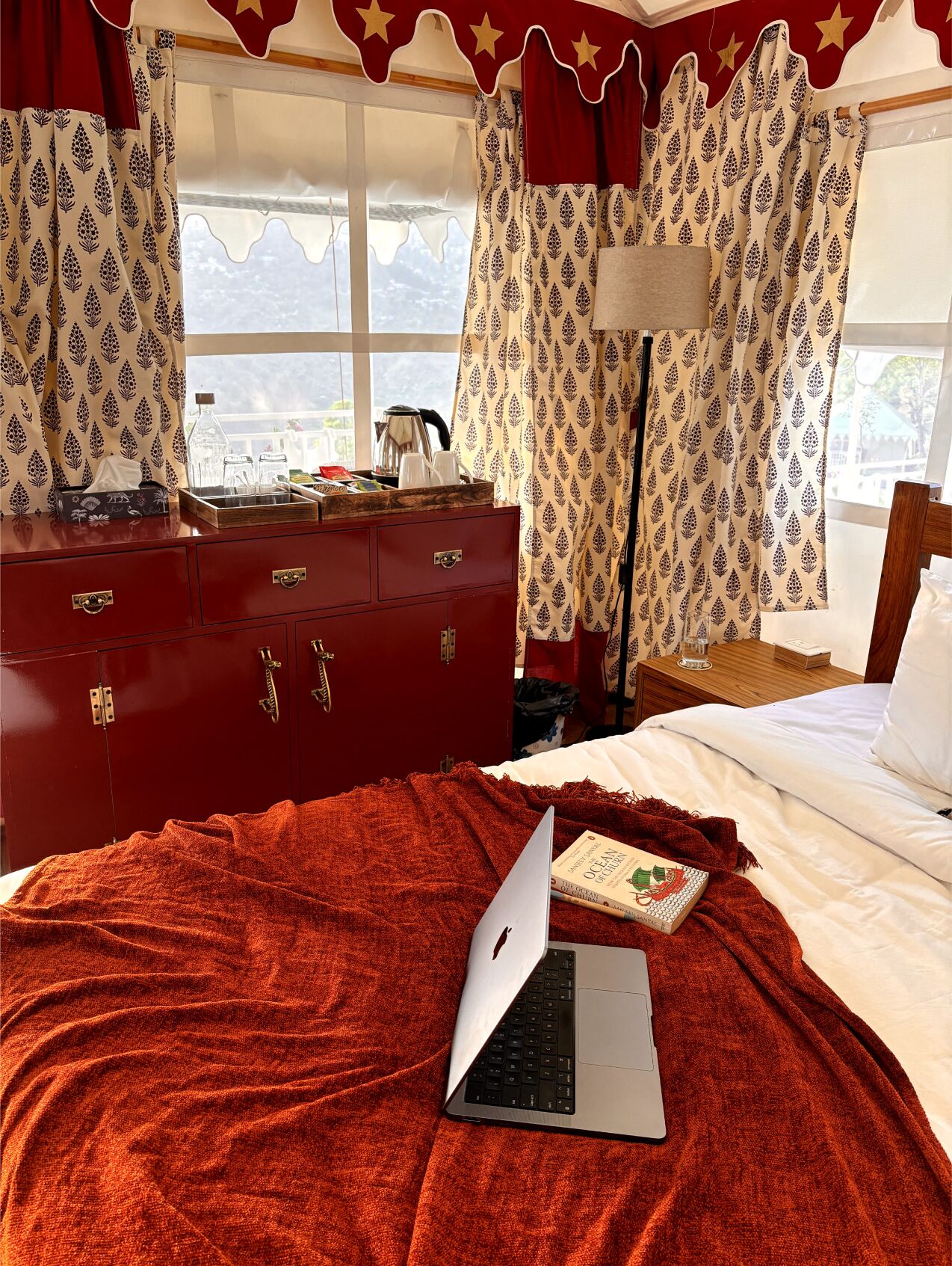 A bedroom with a red dresser, a bed with a red blanket, and a laptop on the bed.