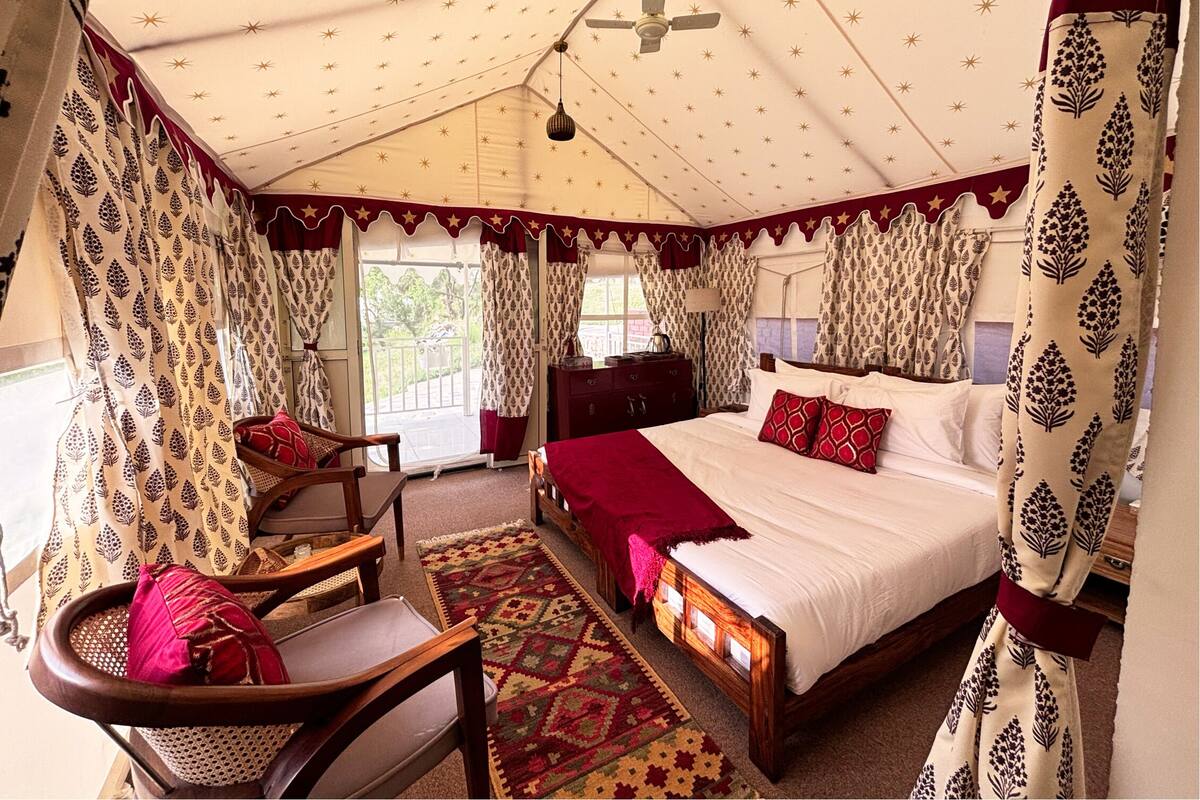 A tent-style room with a bed, a chair, a table, and curtains with a leaf pattern.