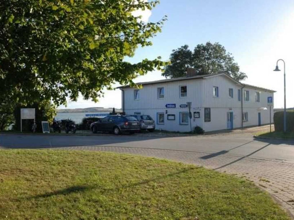 Un bâtiment à deux étages, doté d’un toit plat, un parking où sont garées plusieurs voitures, et une zone herbeuse au premier plan.