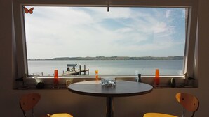 Et værelse med et stort vindue der kigger ud over en sø, et bord med stole, og pynteting på vindueskarmen.