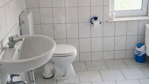 Et badeværelse med et hvidt håndvask, toilet og et vindue.